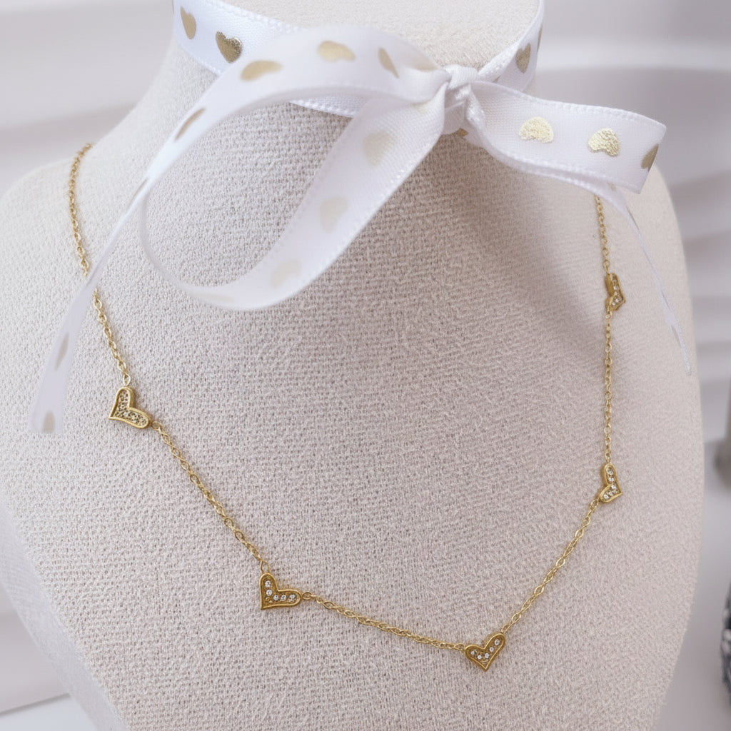 Detalle de collar con corazones dorados y zirconias incrustadas, acero inoxidable.