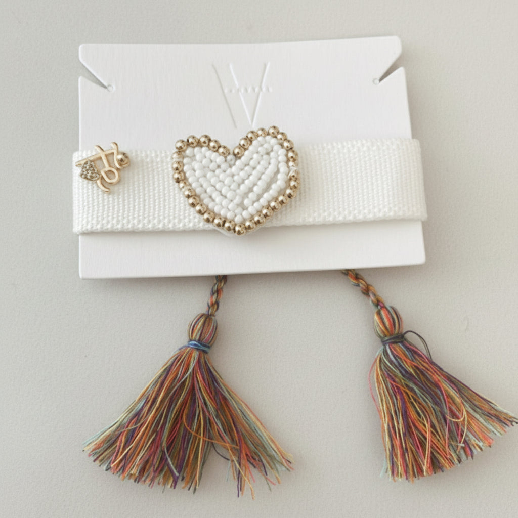 Pulsera artesanal blanca con dije de corazón, símbolo de fe y propósito