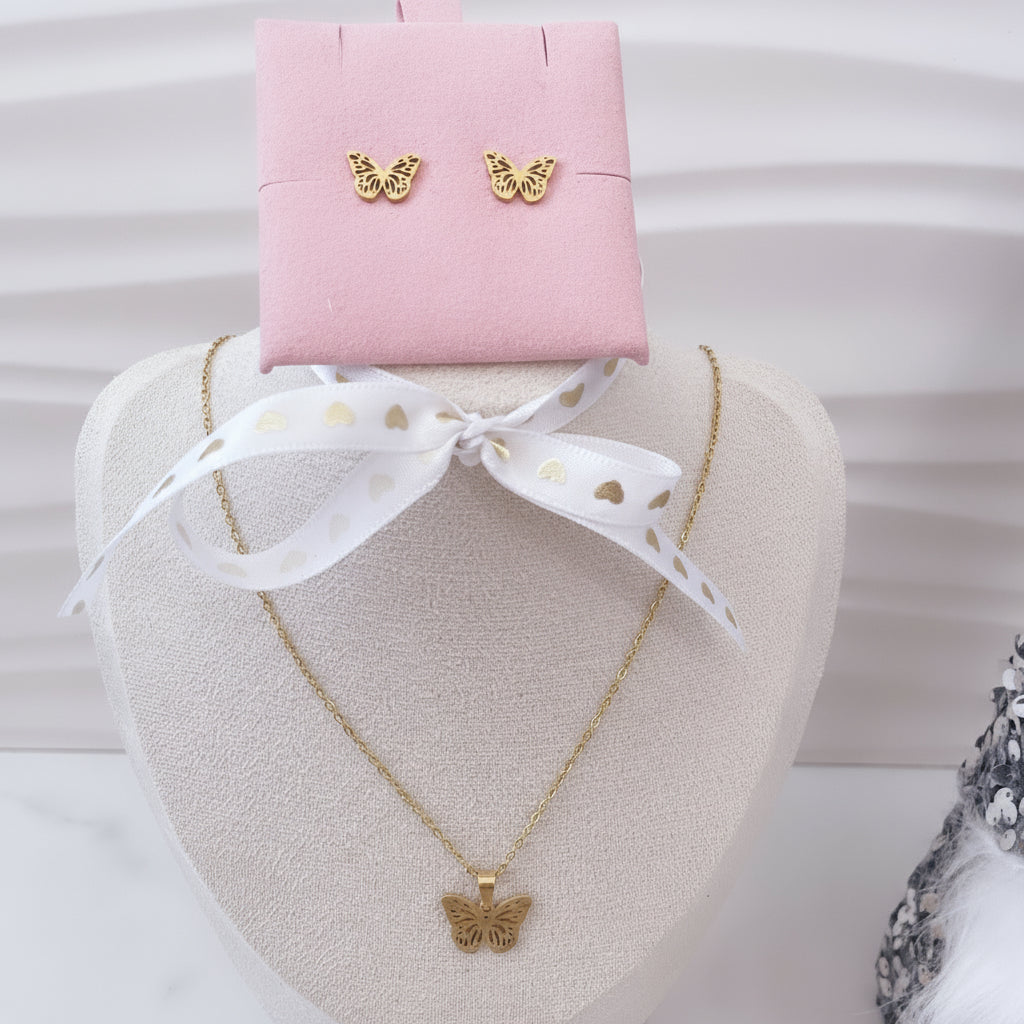 Collar y aretes de mariposas doradas de Vanytel sobre soporte rosa.