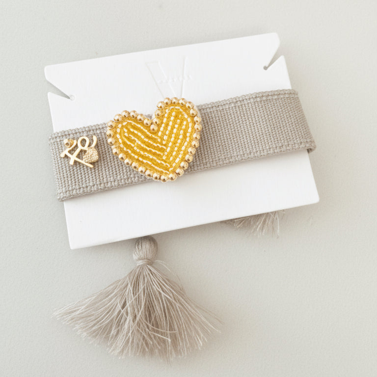 Pulsera hecha a mano gris con dije de corazón dorado, joyería artesanal Vanytel.
