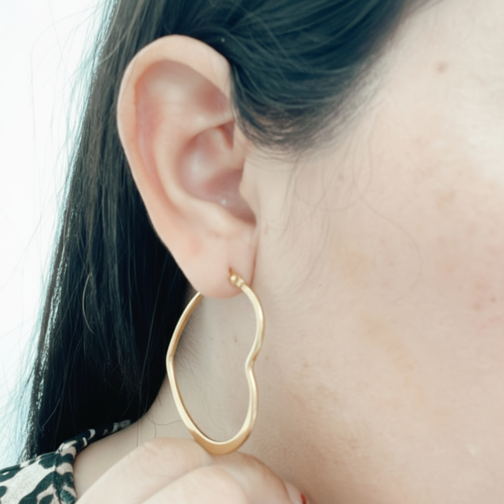 Mujer usando aros hoop dorados con forma de corazón de acero inoxidable Vanytel, perfectos para uso diario o regalo.
